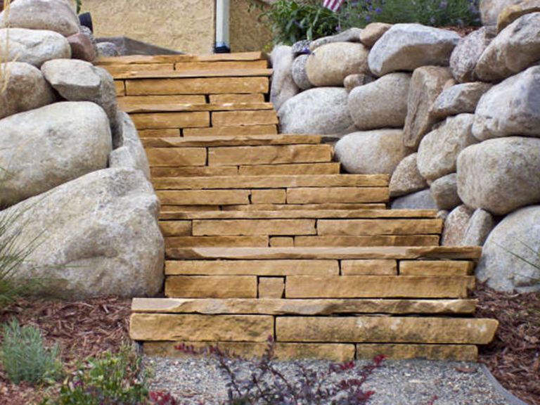 Wooden garden stairs with large boulders on both sides creating a rustic outdoor pathway