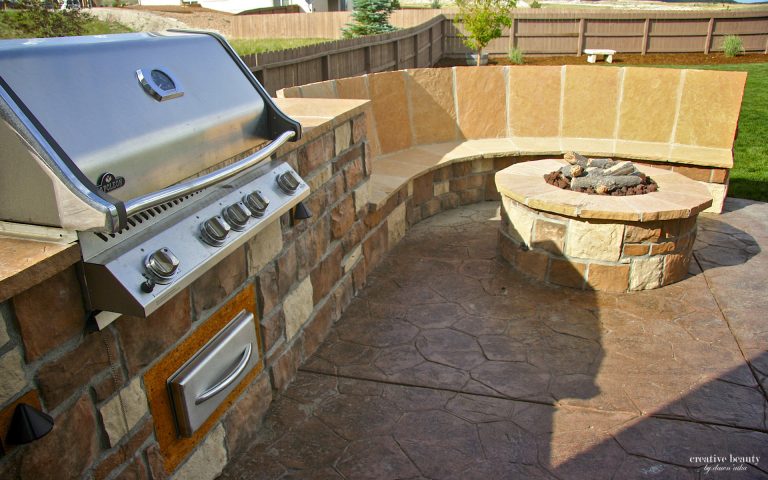 Outdoor patio with built-in stainless steel grill and circular stone fire pit with seating wall