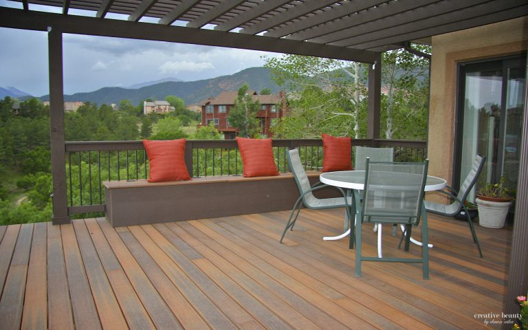 Covered deck with wooden flooring, red planters, seating area, and mountain views