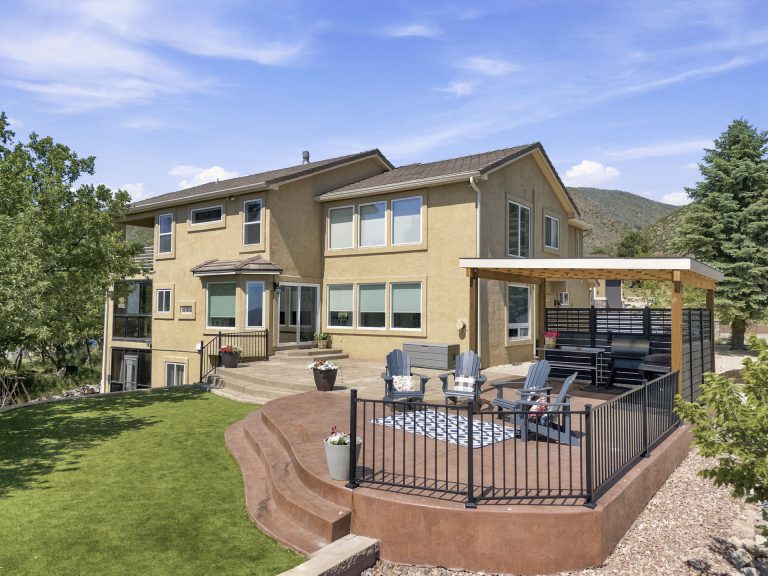 Two-story home with attached deck featuring dark railing and brown composite decking overlooking manicured lawn