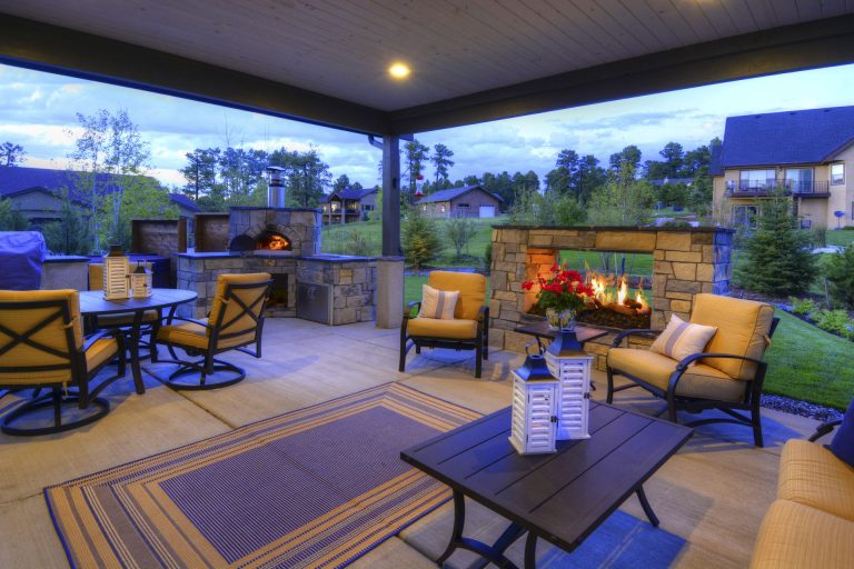 Modern outdoor patio showroom display with furniture, fireplace, and landscaping under covered structure with blue lighting