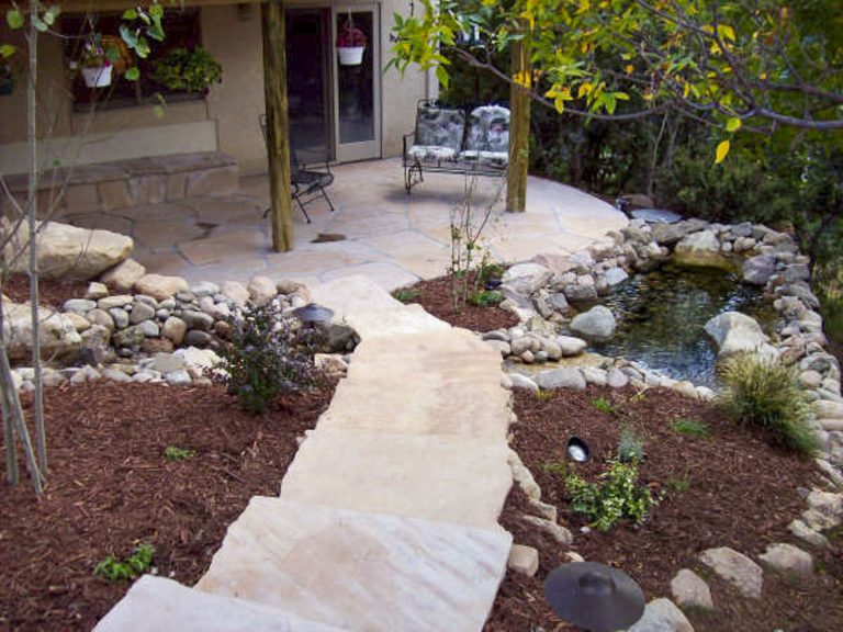 Curved stone pathway with rock borders leading through landscaped yard with mulch beds and plants toward house entrance