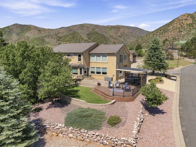 Aerial view of a modern two-story home with yellow exterior, situated on landscaped grounds with mountains in the background