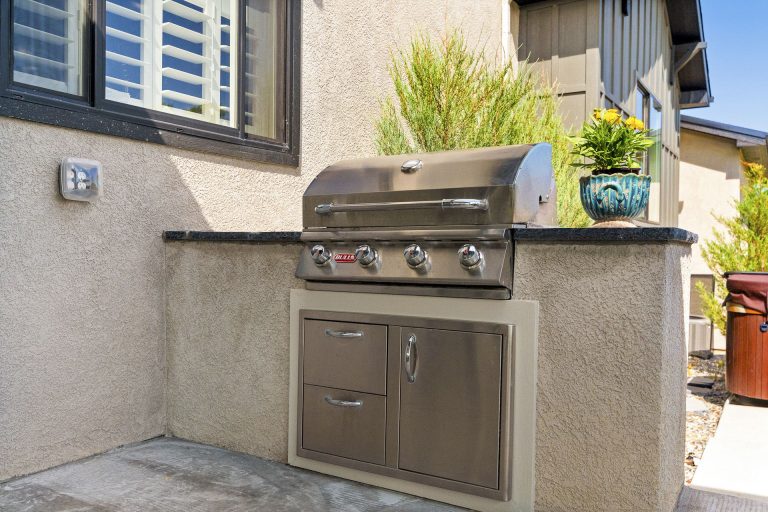 Outdoor kitchen with built-in grill, stainless steel appliances, and stone countertop against house exterior