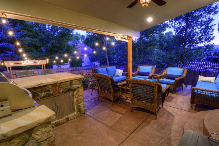 Twilight patio with comfortable seating, outdoor kitchen, string lights, and lounge chairs overlooking the yard