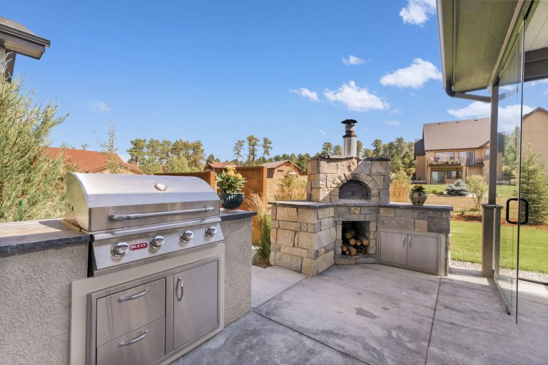Outdoor kitchen patio with built-in grill, pizza oven, and stone countertops under covered pergola with mountain views