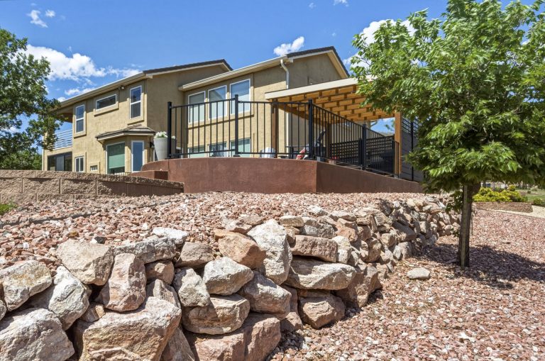 Modern two-story house with brown brick and tan siding, featuring a covered patio and surrounded by desert landscaping with