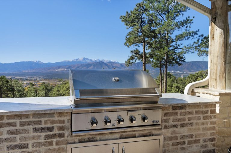 Built-in stainless steel grill on brick outdoor kitchen overlooking lake and mountain views