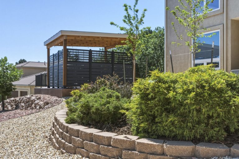Modern black pergola with wooden top in residential garden with curved stone retaining wall and landscaping