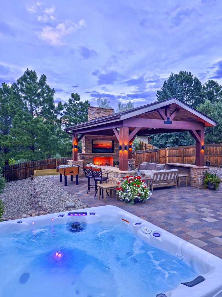 Backyard patio with hot tub, wooden gazebo, dining area, and fire pit at dusk