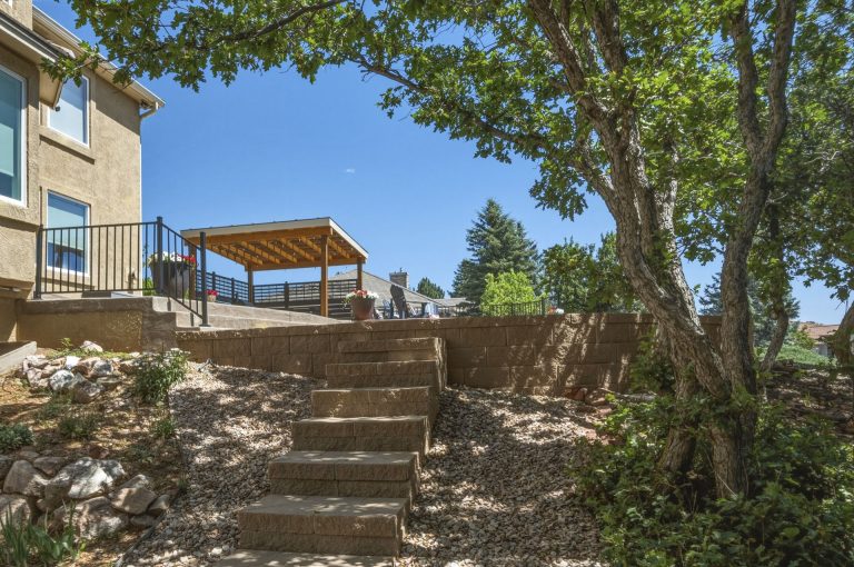 Wooden deck stairs leading up to a house with trees and a gazebo visible in the background