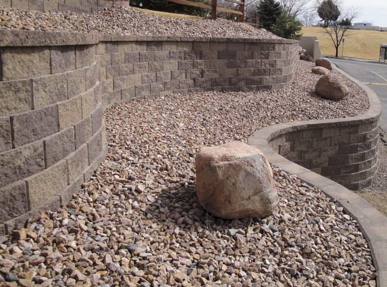Curved retaining wall with gravel landscaping and large decorative boulders along a residential driveway