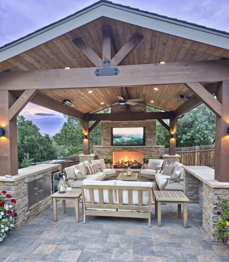 Spacious covered outdoor patio with fireplace, comfortable seating, and dining area under wooden beams