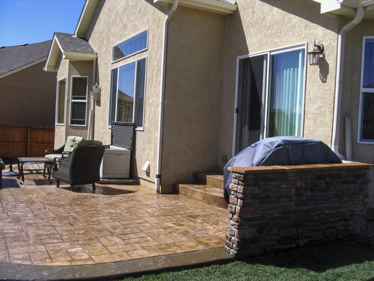 Modern home exterior with brick patio, hot tub, and manicured lawn in sunny residential setting
