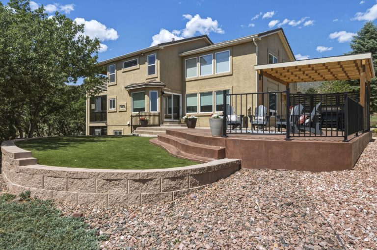 Two-story residential home with brick patio, pergola, landscaped yard and blue sky