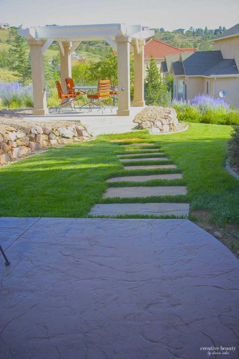 Modern backyard garden with stone pathway, green lawn, pergola, and landscaping leading to residential home