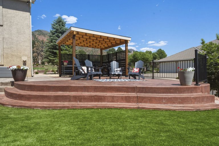 Modern wooden pergola with seating area on brick patio overlooking manicured lawn and residential landscape
