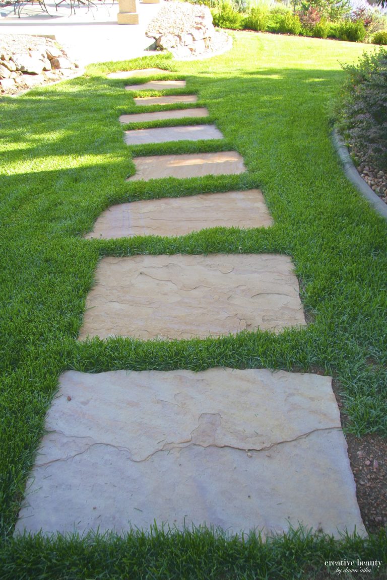 Stepping stone pathway made of rectangular pavers crossing through green lawn in a residential garden