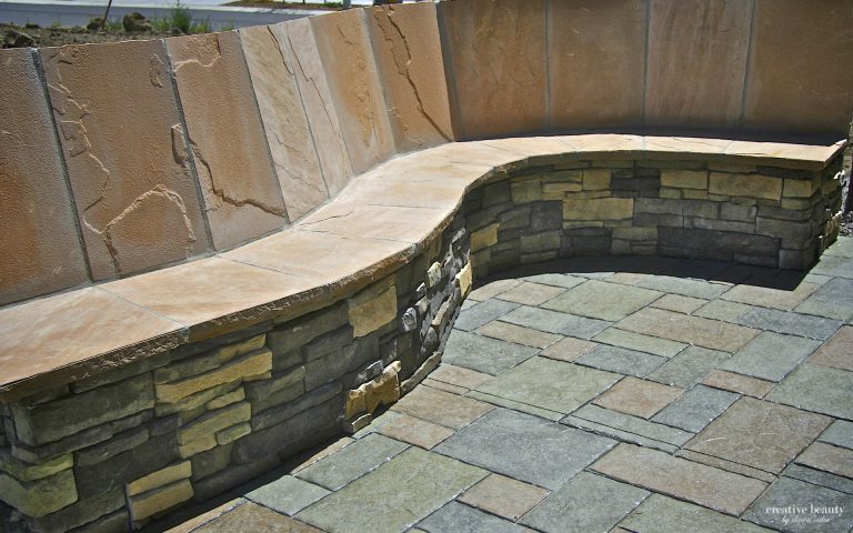 Curved stone retaining wall with patterned masonry blocks and wooden cap detail at construction site