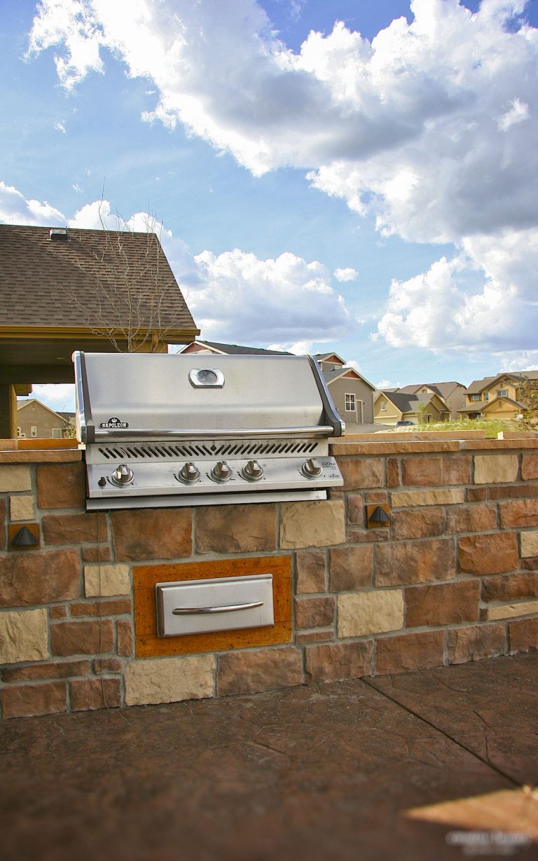 Stainless steel built-in grill mounted on a brick outdoor kitchen counter with blue sky and clouds