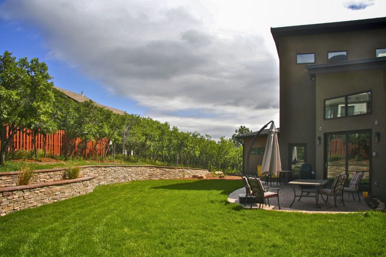 Modern house with large backyard featuring green lawn, wooden fence, trees, and dramatic cloudy sky