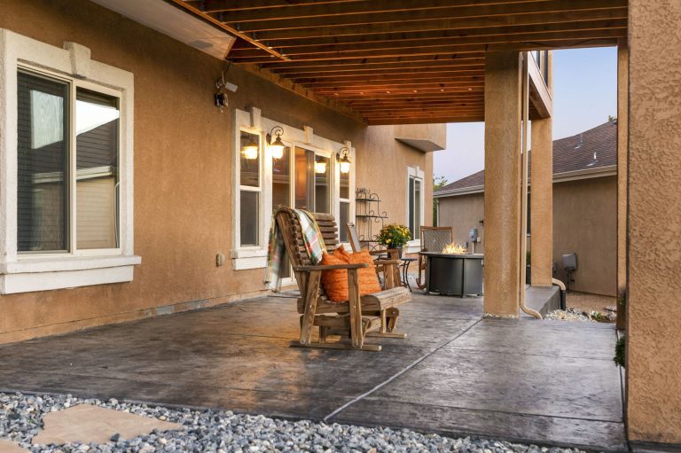 Covered patio area with wooden ceiling, concrete floor, wooden chairs, and open doorways leading to residential spaces