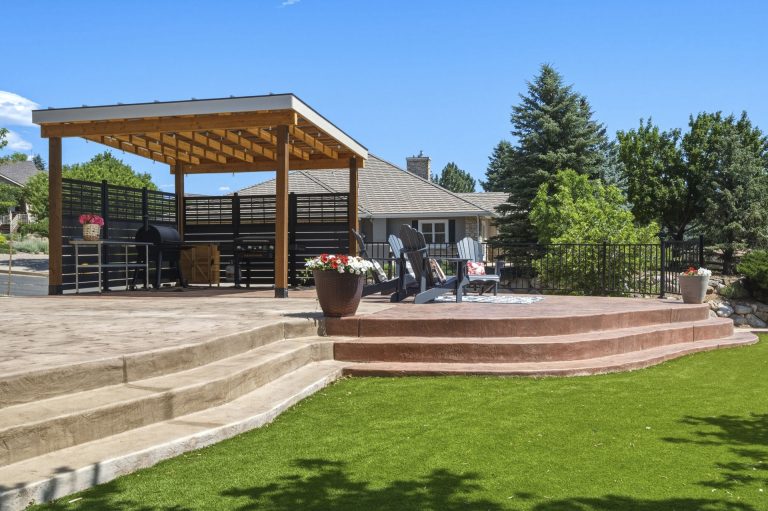 Modern backyard patio with wooden pergola, built-in seating, and raised planter bed surrounded by manicured lawn and