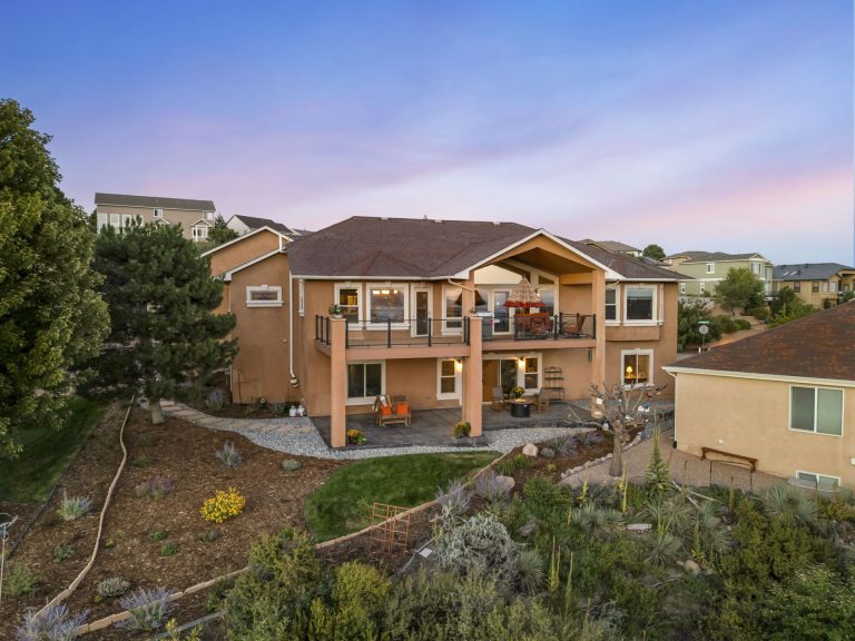Modern two-story brick home with large windows on hillside surrounded by landscaping and trees