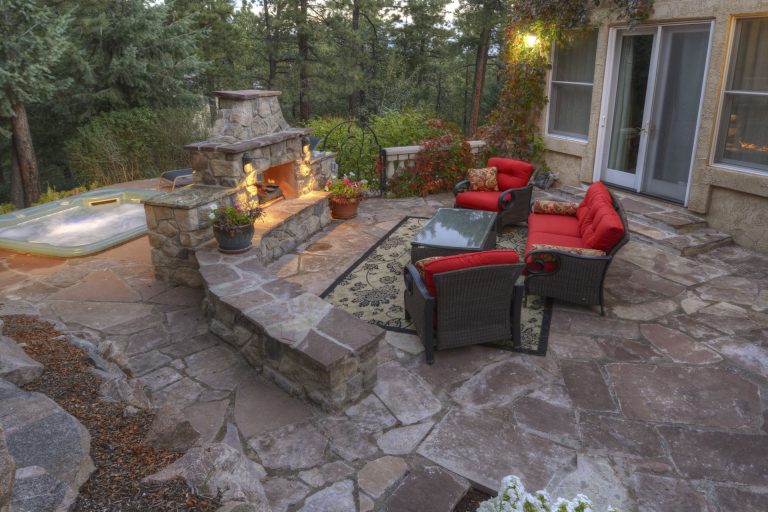 Backyard patio with stone fireplace, comfortable seating, and hot tub at dusk