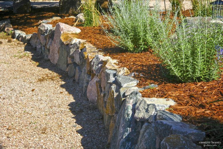 Rustic stone border edging along a gravel garden path with mulch and green plants