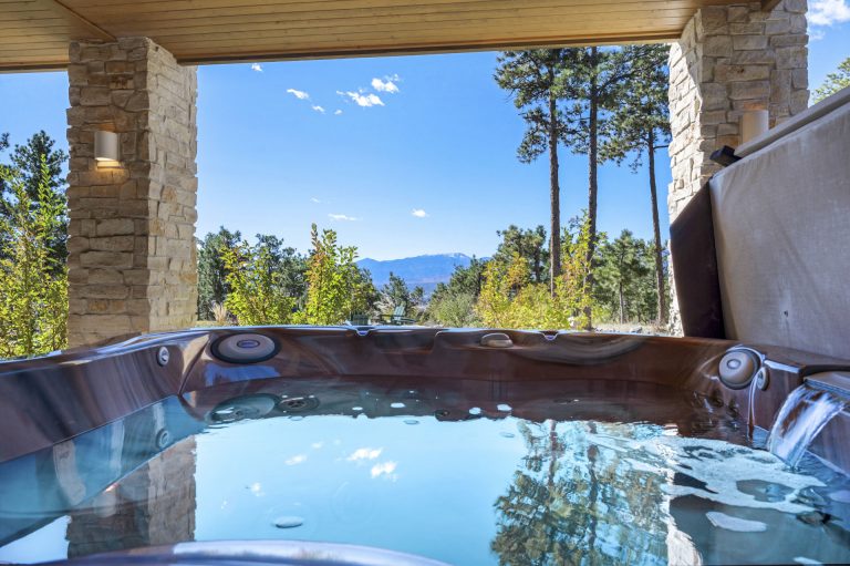 Luxury hot tub on a stone patio overlooking forested mountains under clear blue sky