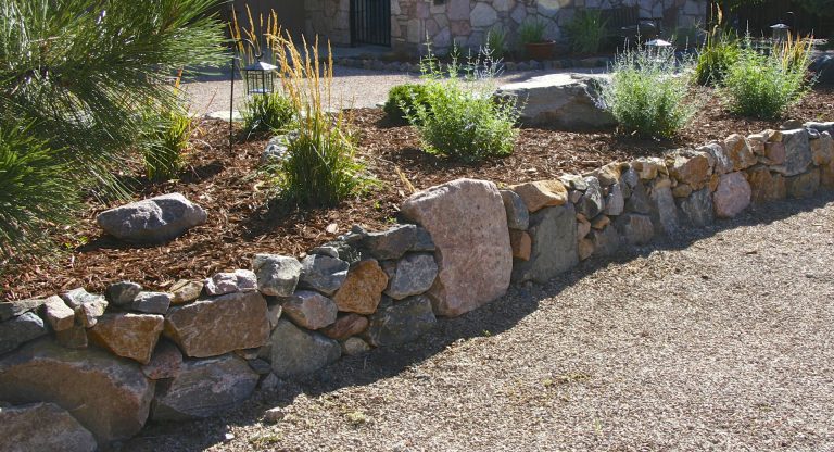 Rustic stone retaining wall with ornamental grasses along a gravel pathway in a landscaped garden