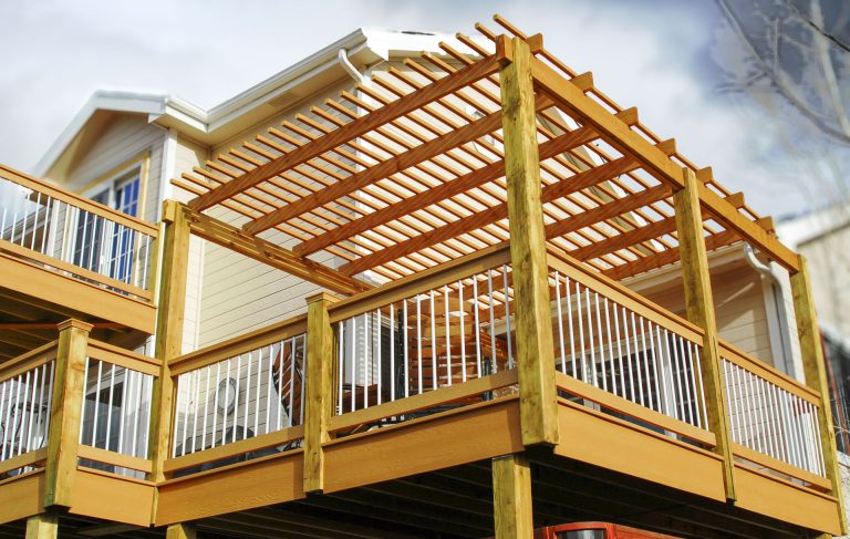 Wooden pergola attached to yellow elevated deck with white railings and stairs