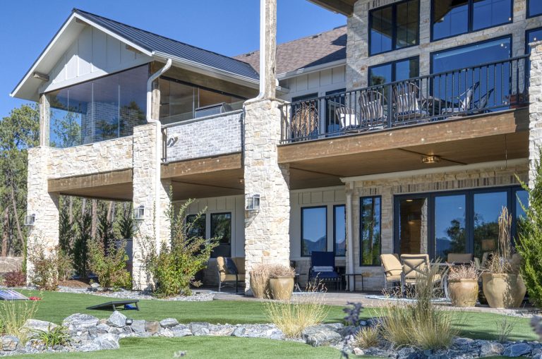 Modern two-story home with stone pillars, large windows, wooden decks, and manicured landscaping