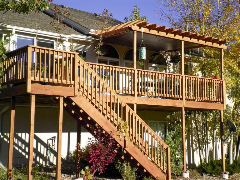 Elevated wooden deck with pergola and stairs leading down to backyard patio area