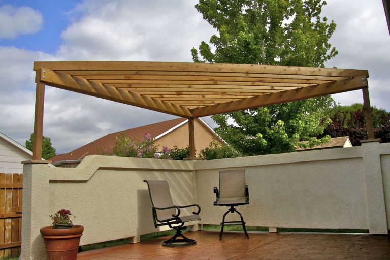 Wooden pergola with louvered roof over patio seating area with recliners and privacy screen