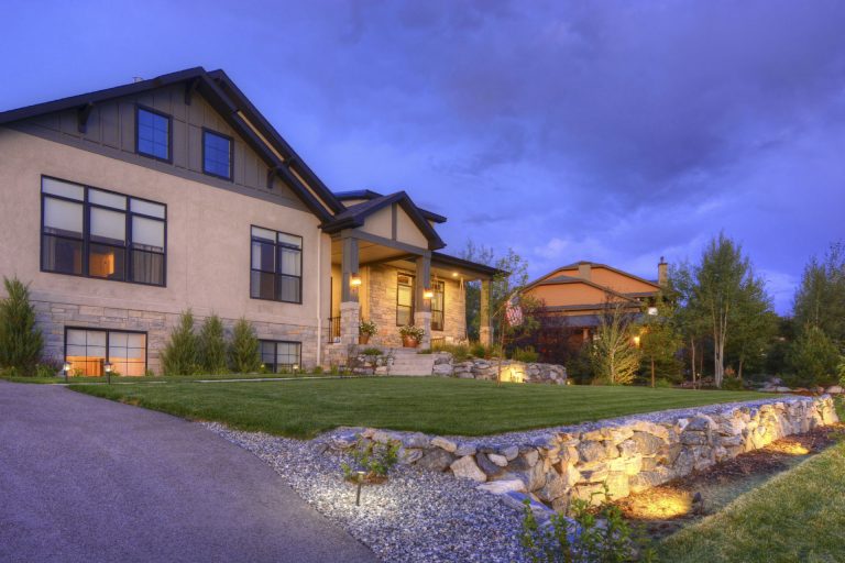 Luxury home exterior at dusk with illuminated landscape lighting, stone pathway, and manicured gardens