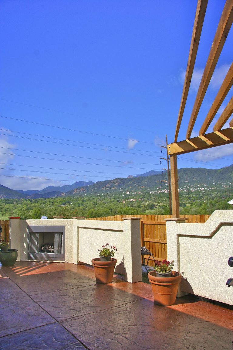 Rooftop patio with wooden pergola, potted plants, and mountain valley views under clear blue sky