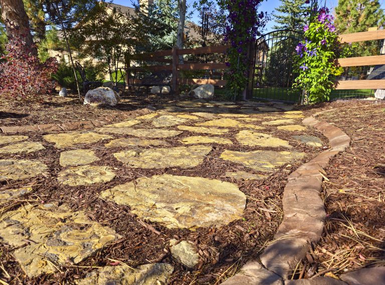 Rustic stone pathway winding through a wooded garden with trees and mulch landscaping