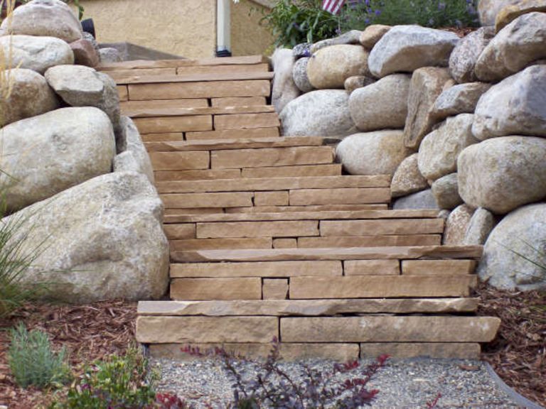 Wooden steps leading upward flanked by stacked boulders on both sides in a garden landscape