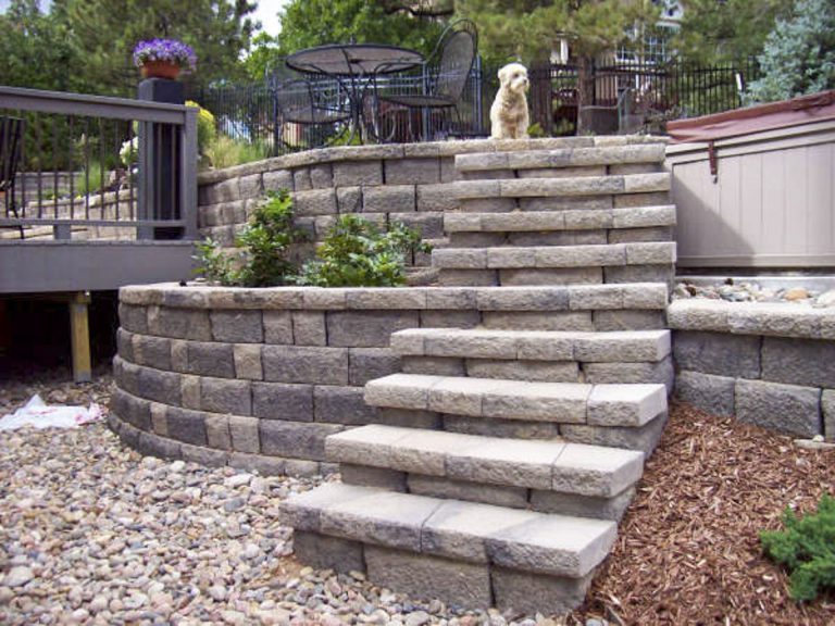 Outdoor stone steps leading up to a wooden deck with metal railing and landscaping