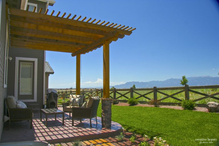 Wooden pergola with seating area on brick patio overlooking green lawn and mountain landscape