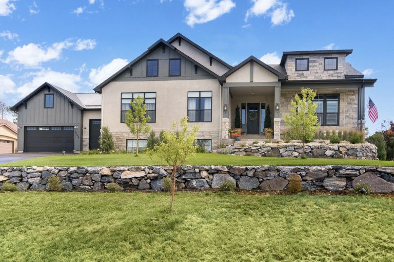 Modern two-story home with stone landscaping, manicured lawn, and attached garage on a sunny day