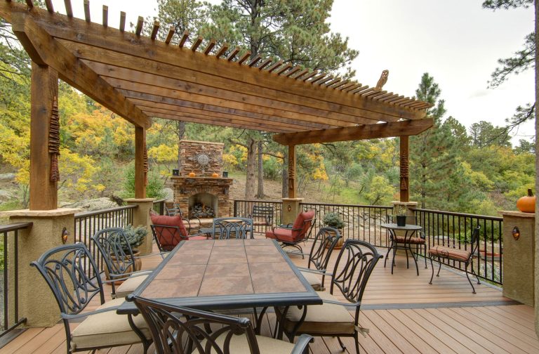 Wooden pergola with dining table and chairs on a spacious deck overlooking landscaped grounds