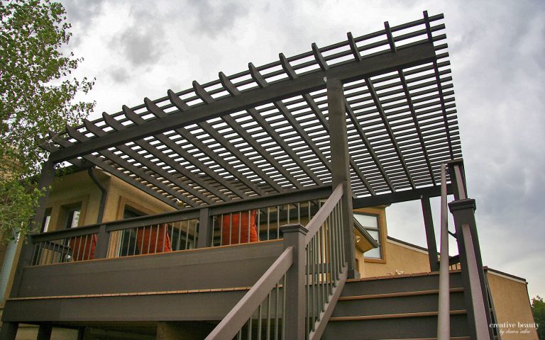 Modern wooden pergola attached to a residential deck with stairs and railings under a cloudy sky