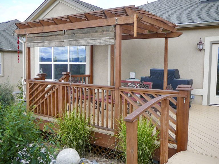 Wooden pergola attached to house with railing and outdoor furniture on patio