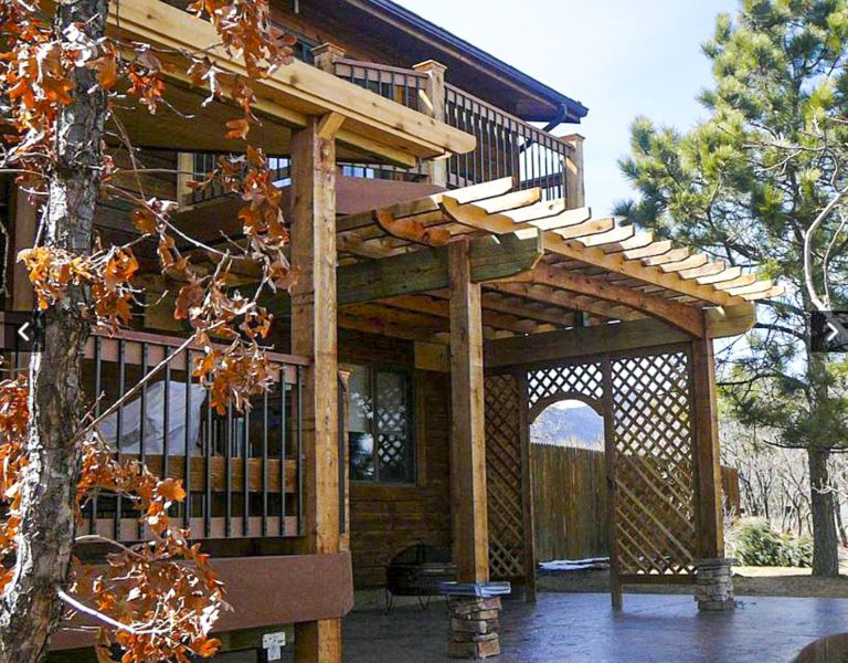 Wooden pergola structure with lattice panels and climbing ivy attached to a rustic house exterior
