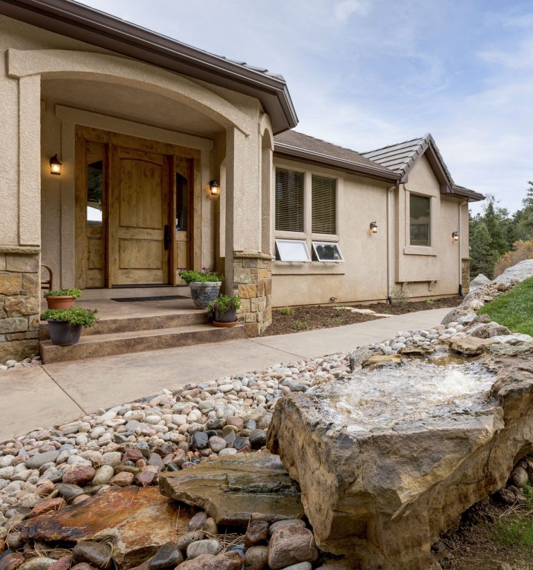 Modern beige house with stone accents, wooden door, and landscaped front yard with decorative rocks
