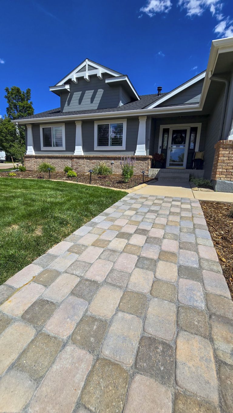 Modern two-story home with blue siding, brick foundation, and decorative paver driveway under clear blue sky
