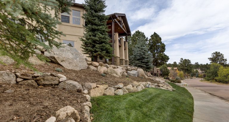 Modern house with stone foundation and ivy-covered walls on sloped landscaped yard with green lawn and trees